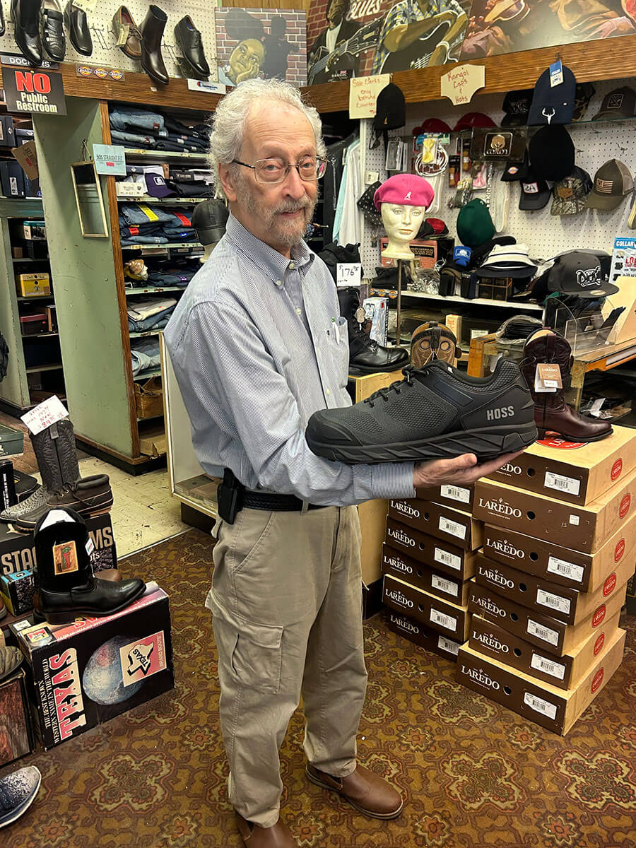 A black HOSS work shoe held up in front of boot boxes and casual shoes at Kornfeld's.