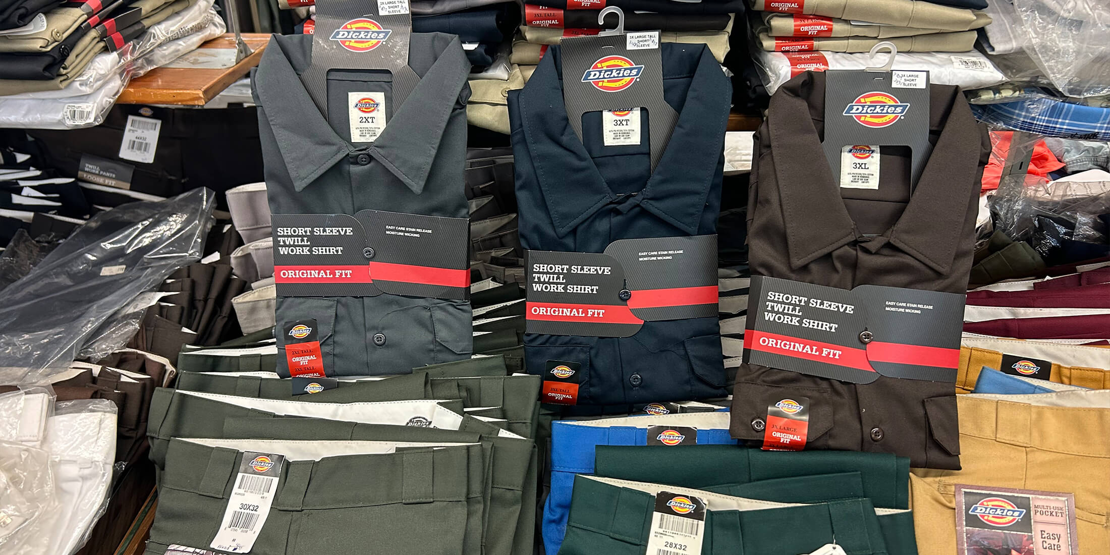 Folded Dickies short-sleeve twill work shirts and work pants stacked on a table at Kornfeld's Department Store.